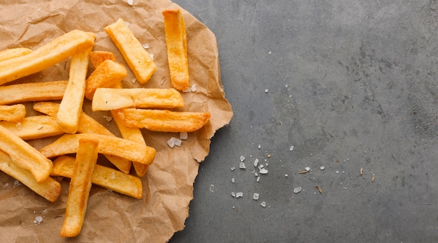 Vista dall'alto di patatine fritte su carta con sale e copia spazio