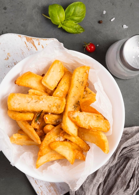 Vista dall'alto di patatine fritte sulla piastra con saliera ed erbe aromatiche