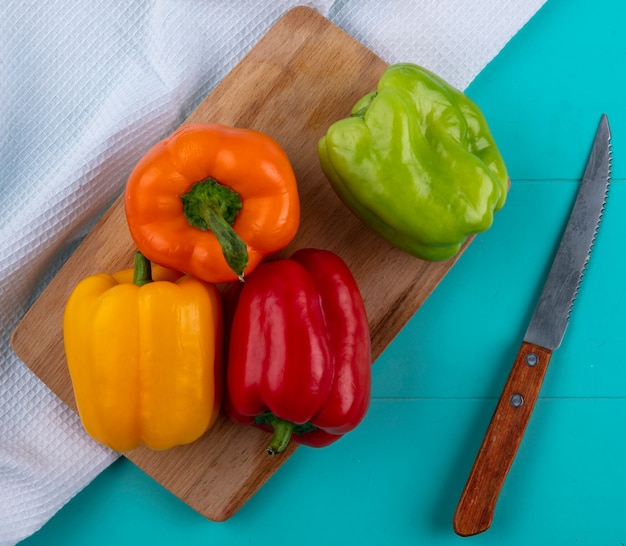 Vista dall'alto di peperoni colorati su un tagliere con un coltello su una superficie turchese