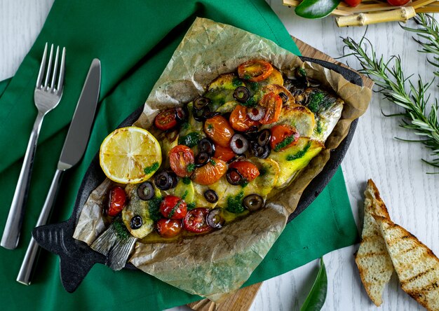 vista dall'alto di pesce arrosto condita con patate, pomodorini, olive e limone