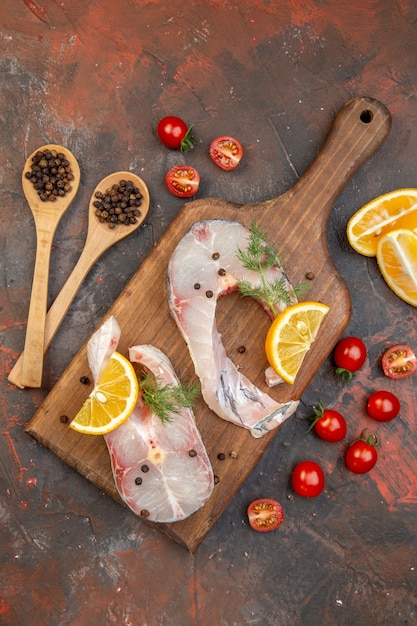 Vista dall'alto di pesce crudo e pepe sul tagliere di legno fette di limone pomodori sulla superficie di colore della miscela