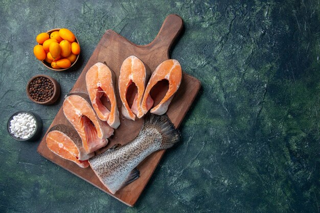 Vista dall'alto di pesce crudo fresco sul tagliere di legno e peperoni kumquat sul tavolo colori mix scuri