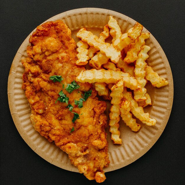 Vista dall'alto di pesce e patatine fritte sulla piastra con erbe aromatiche