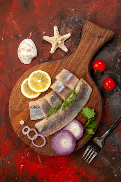 Vista dall'alto di pesce fresco a fette con anelli di cipolla su sfondo scuro