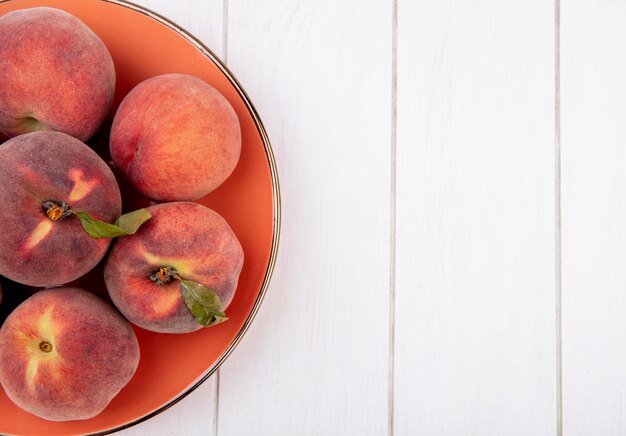 Vista dall'alto di pesche fresche e succose onn piatto arancione su bianco con copia spazio