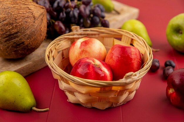 Vista dall'alto di pesche fresche e succose su un secchio con cocco su una tavola da cucina in legno su uno sfondo rosso