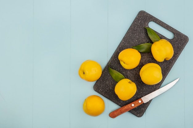 Vista dall'alto di pesche gialle fresche su un tagliere da cucina con coltello su uno sfondo blu con spazio di copia