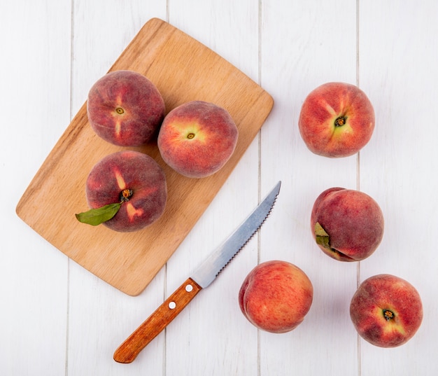 Vista dall'alto di pesche su una tavola di cucina in legno con coltello con pesche isolato su una superficie bianca