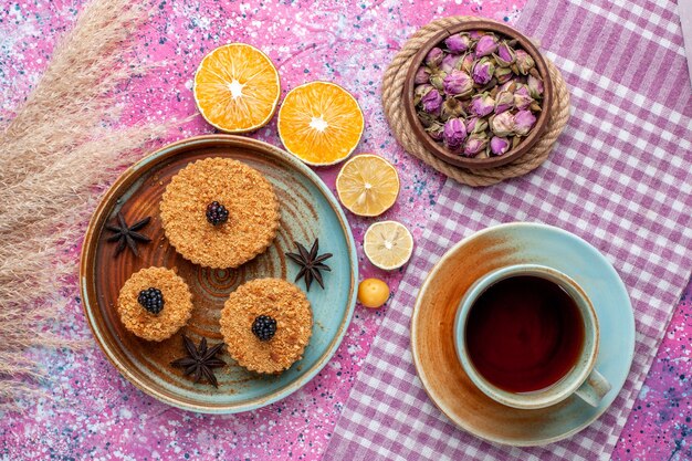 Vista dall'alto di piccole deliziose torte con fette d'arancia e tè sulla superficie rosa