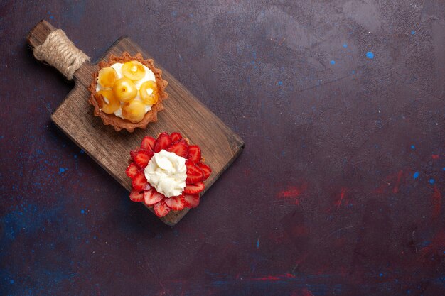 Vista dall'alto di piccole torte cremose con frutta a fette su superficie scura