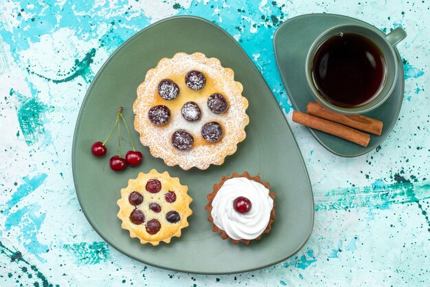 Vista dall'alto di piccole torte deliziose e cotte insieme a tè alla cannella con frutta su torta azzurra, tè dolce cuocere frutta torta