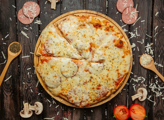 vista dall'alto di pizza ai peperoni con salsiccia, salsa di pomodoro, formaggio ed erbe spruzza