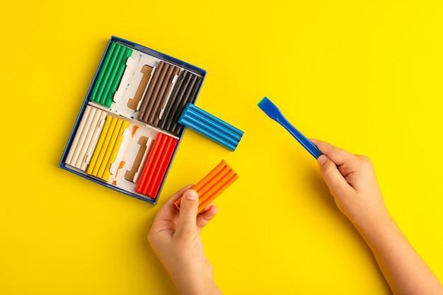 Vista dall'alto di plastiline colorate bambino che lavora e gioca con esso sulla scuola per bambini con foto a colori parete gialla