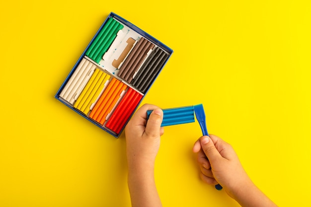 Vista dall'alto di plastiline colorate bambino che lavora e gioca con esso sulla scuola per bambini con foto a colori parete gialla