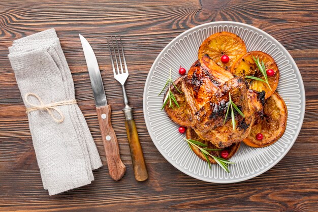 Vista dall'alto di pollo al forno e fette d'arancia sul piatto con posate e tovagliolo