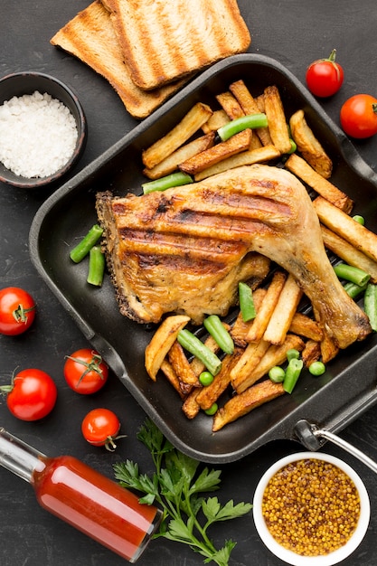 Vista dall'alto di pollo al forno e patate in padella con pomodori e pane tostato