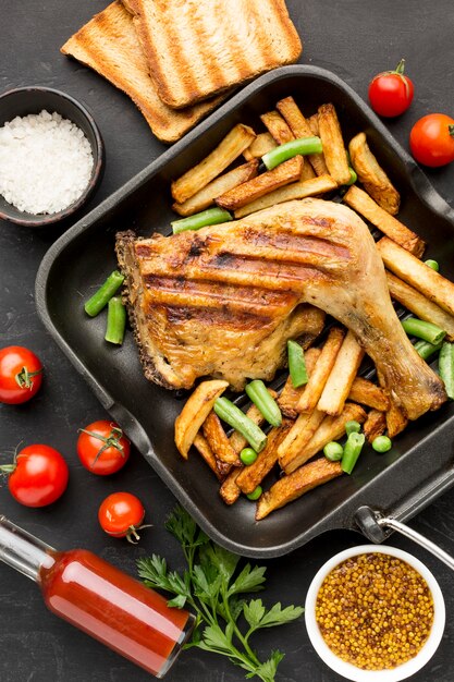 Vista dall'alto di pollo al forno e patate in padella con pomodori e pane tostato