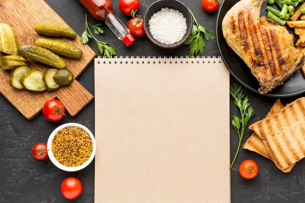 Vista dall'alto di pollo al forno e patate sul piatto con sottaceti e blocco note in bianco