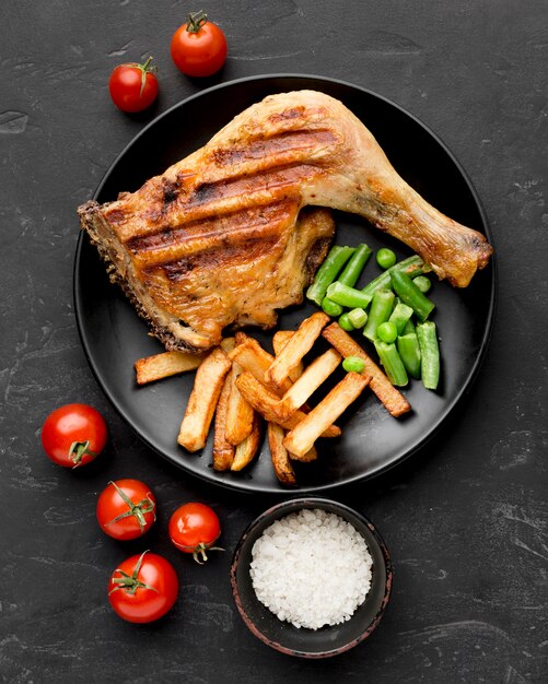 Vista dall'alto di pollo al forno e patate sulla piastra con i pomodori