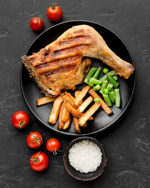 Vista dall'alto di pollo al forno e patate sulla piastra con i pomodori