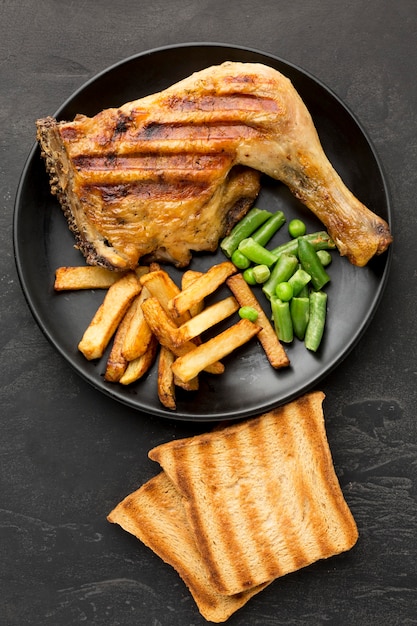 Vista dall'alto di pollo al forno e patate sulla piastra con pane tostato