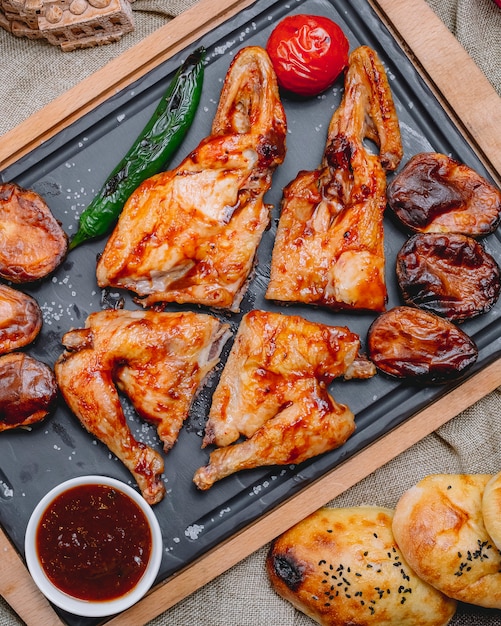 Vista dall'alto di pollo al forno tabacco in salsa con patate pomodoro e pepe con salsa su un vassoio