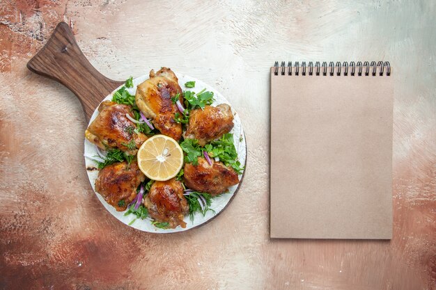 Vista dall'alto di pollo pollo erbe cipolla limone sulla lavagna accanto al taccuino crema