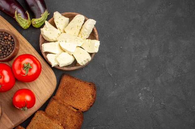 Vista dall'alto di pomodori freschi al buio. pagnotte di pane e formaggio bianco su fondo nero