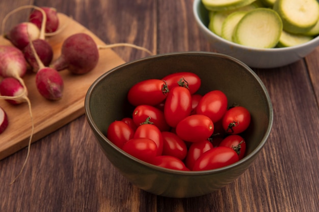 Vista dall'alto di pomodori freschi su una ciotola con ravanelli su una tavola da cucina in legno con zucchine tritate su una ciotola su una superficie di legno