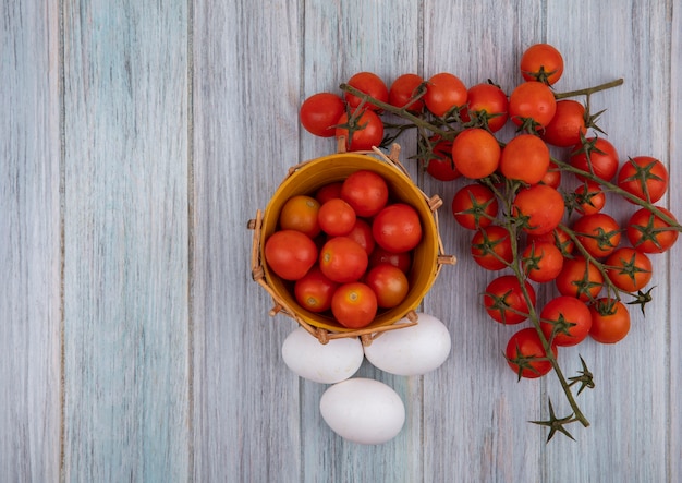 Vista dall'alto di pomodori maturi su un secchio con pomodori a grappolo e uova isolate su uno sfondo di legno grigio con spazio di copia