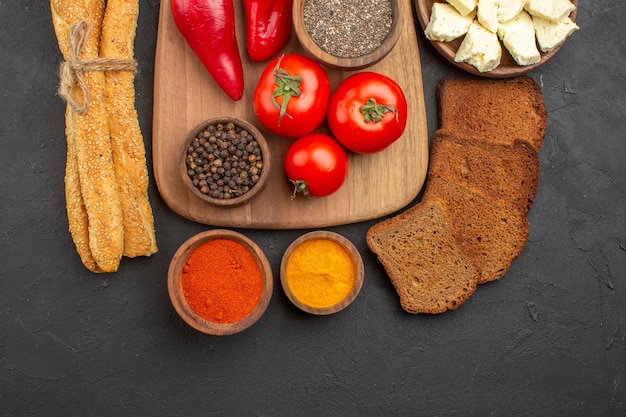 Vista dall'alto di pomodori rossi freschi con condimenti formaggio e pane su nero