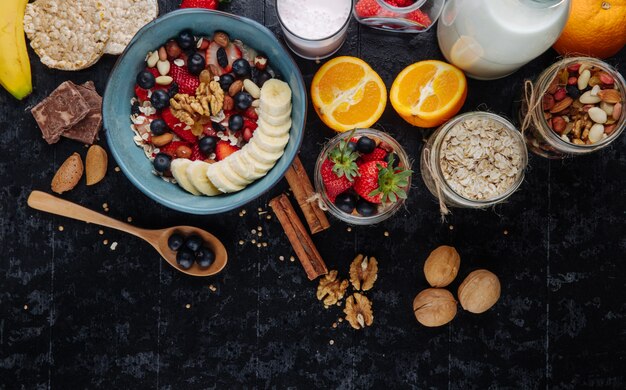 Vista dall'alto di porridge di farina d'avena con fragole mirtilli banane frutta secca e noci in una ciotola di ceramica e vasetti di vetro con noci miste avena e fiocchi di avena sul tavolo