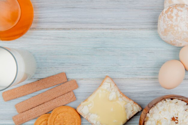 vista dall'alto di prodotti lattiero-caseari come ricotta di latte spalmata sulla fetta di pane con biscotti burro panpepato uova sul tavolo di legno con spazio di copia