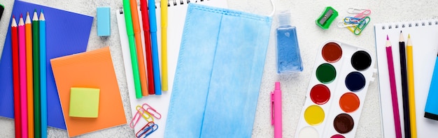 Vista dall'alto di ritorno a materiale scolastico con maschera e acquerello