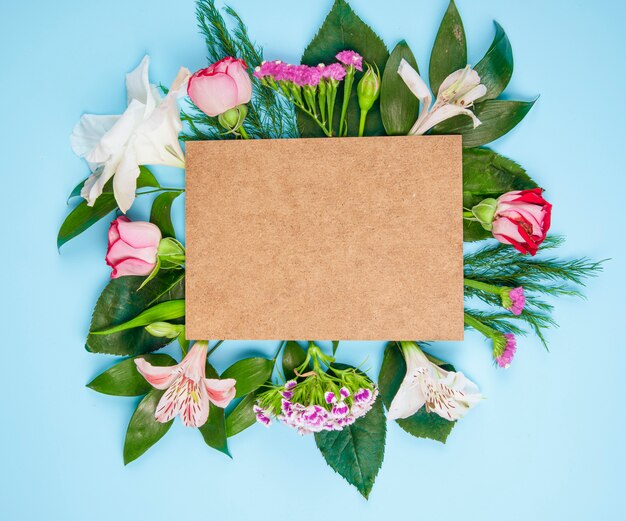 Vista dall'alto di rose di colore rosa e fiori di alstroemeria con garofano turco con un foglio di carta marrone su sfondo blu