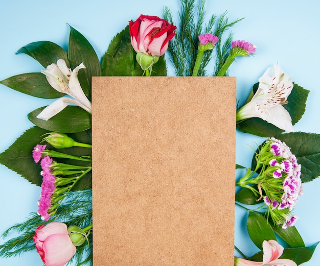 Vista dall'alto di rose rosa e bianche e fiori di alstroemeria con garofano turco e statice con un foglio di carta marrone su sfondo blu