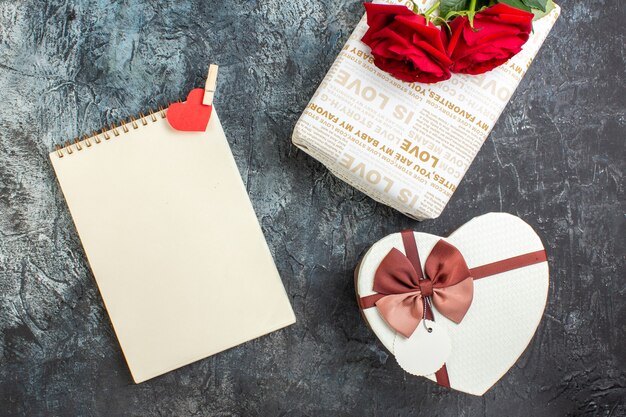 Vista dall'alto di rose rosse e bellissime scatole regalo quaderno a spirale con accessorio cuore su sfondo scuro ghiacciato con spazio libero