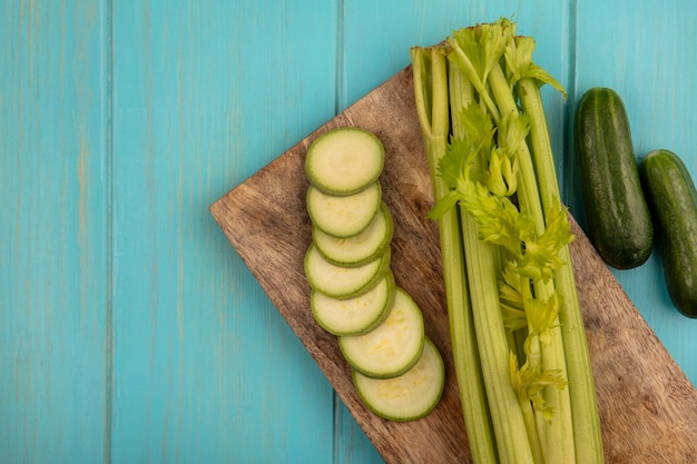 Vista dall'alto di sedano fresco con zucchine tritate su una tavola da cucina in legno con cetrioli isolato su una parete in legno blu con spazio di copia