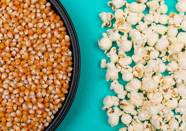 Vista dall'alto di semi di popcorn in padella di metallo nero a sinistra e preparato a destra su superficie orizzontale blu