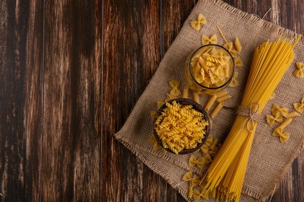 Vista dall'alto di spaghetti crudi con pasta cruda su un tovagliolo beige su una superficie di legno