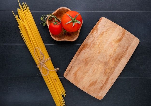 Vista dall'alto di spaghetti crudi con pomodori e lavagna su una superficie nera