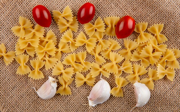 Vista dall'alto di spaghetti crudi con pomodorini e aglio su un tovagliolo beige