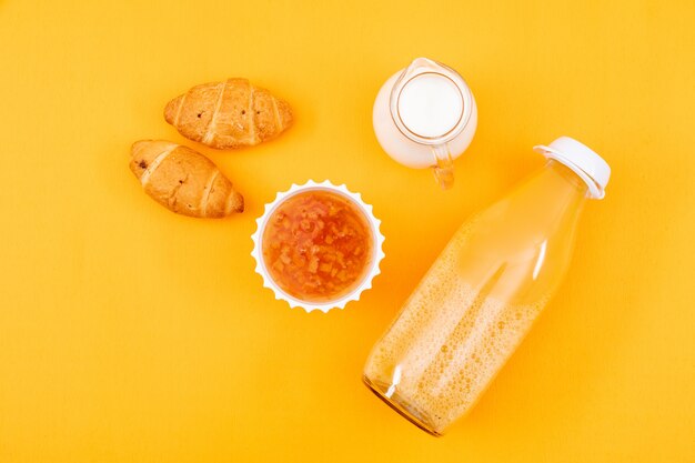 Vista dall'alto di succo con cornetti e marmellata, latte su superficie gialla orizzontale