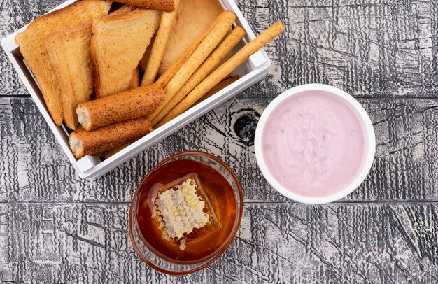 Vista dall'alto di toast con cracker in cassa con miele e yogurt su superficie bianca orizzontale