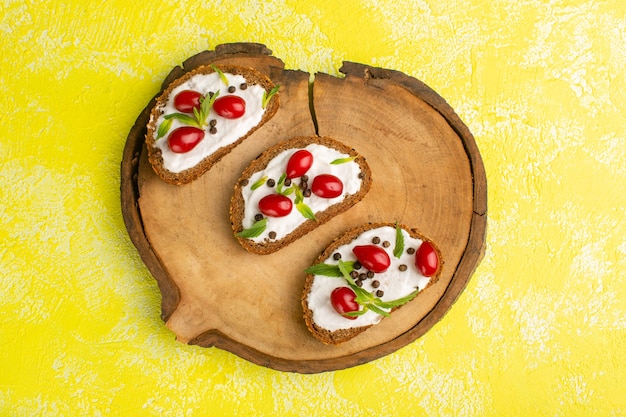 Vista dall'alto di toast di pane con panna acida e cornioli sulla superficie gialla