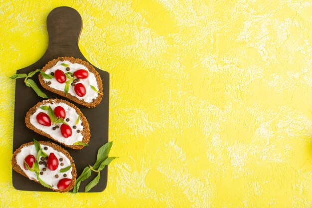 Vista dall'alto di toast di pane con panna acida e cornioli sulla superficie gialla