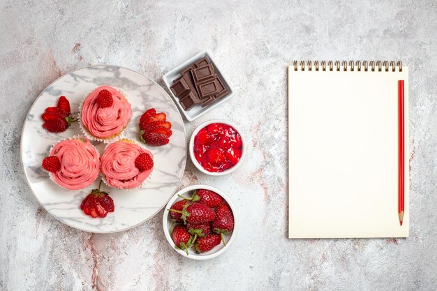 Vista dall'alto di torte alla fragola rosa con crema e tazza di tè sulla superficie bianca