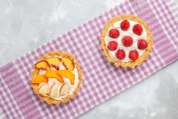 Vista dall'alto di torte cremose con crema bianca squisita e fragole affettate pesche albicocche sulla scrivania leggera, torta di frutta crema cuocere