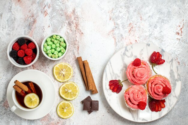 Vista dall'alto di torte di fragole rosa con confetture e tè sulla superficie bianca