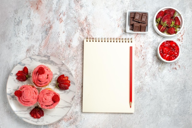 Vista dall'alto di torte di fragole rosa con marmellata e barrette di cioccolato sulla superficie bianca